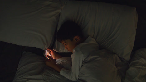 Young-Boy-In-Bedroom-At-Home-Lying-In-Bed-Using-Mobile-Phone-To-Text-Message-At-Night-2